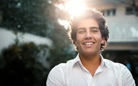 smiling man with curly hair who got a tooth crown in Huntington NY