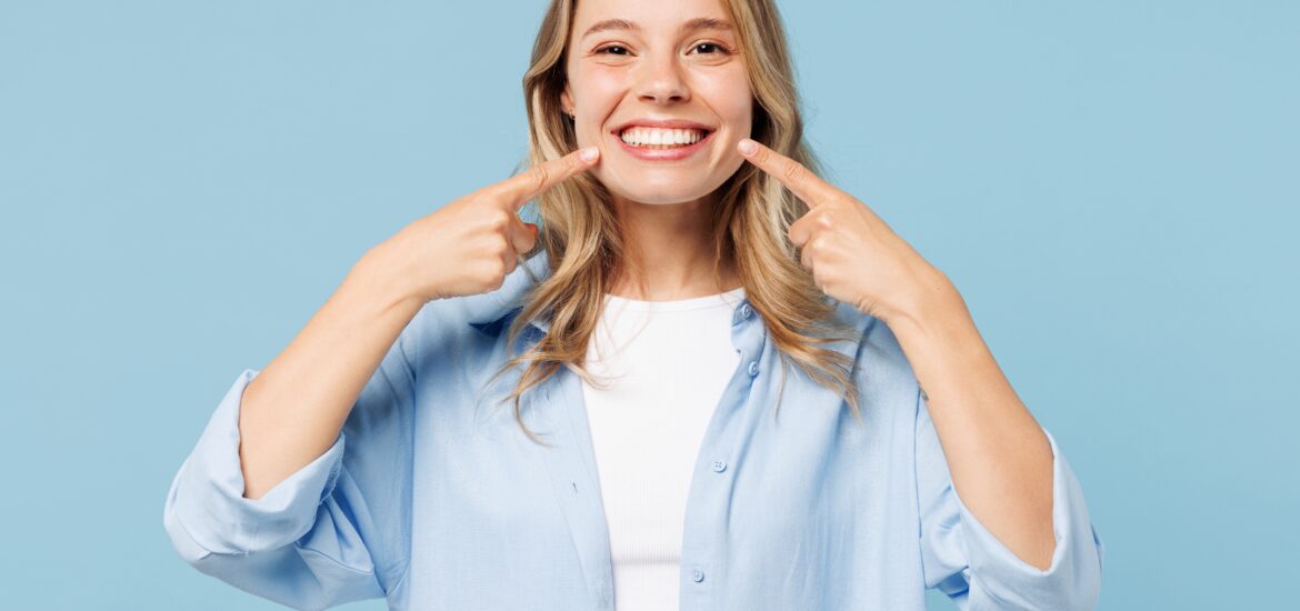 Young smiling woman pointing index fingers to opened mouth, showing professionally whitening teeth