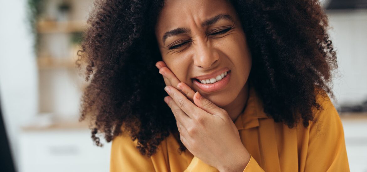 Young African American woman suffering from strong jaw pain, touching her cheek because of acute pain from Teeth grinding