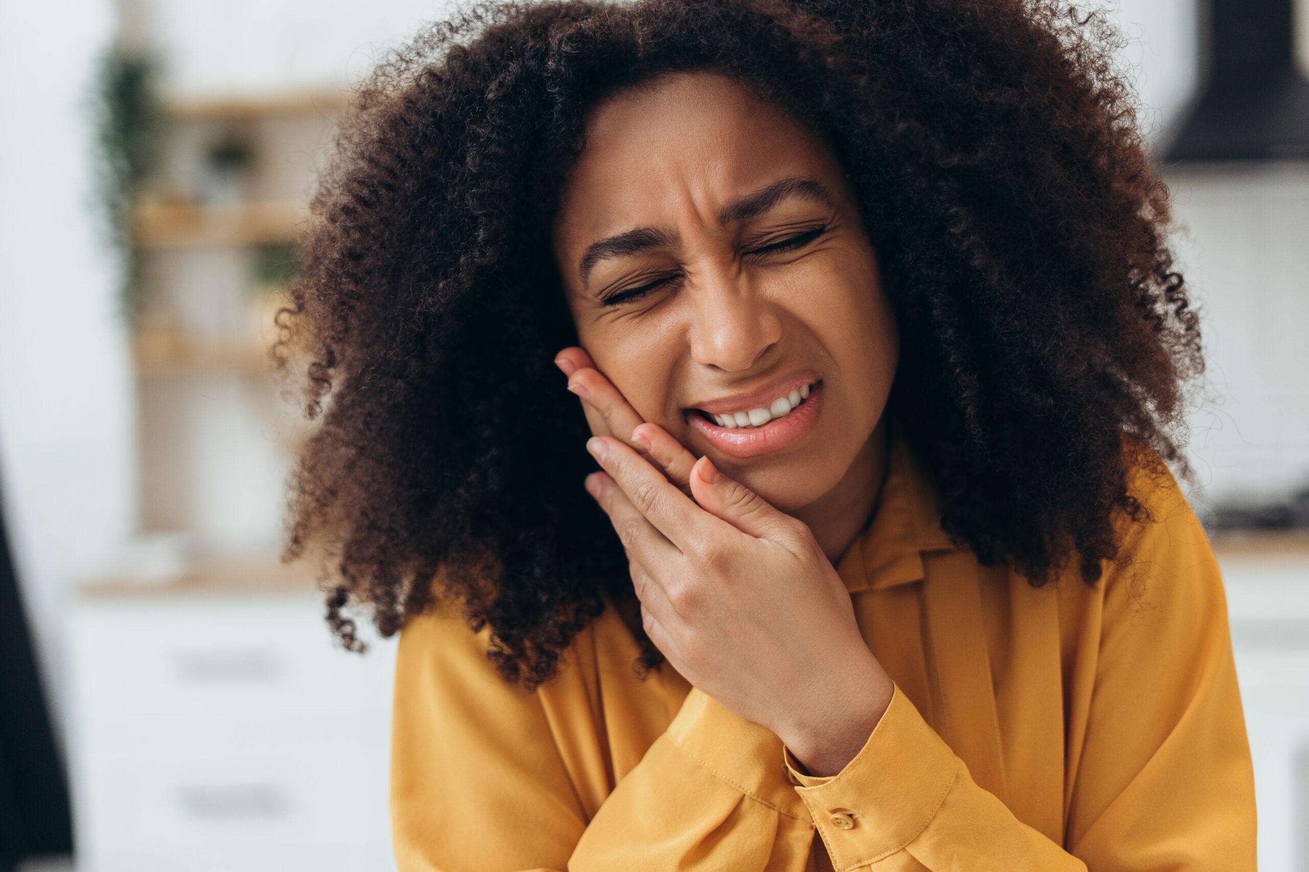 Young African American woman suffering from strong jaw pain, touching her cheek because of acute pain from Teeth grinding