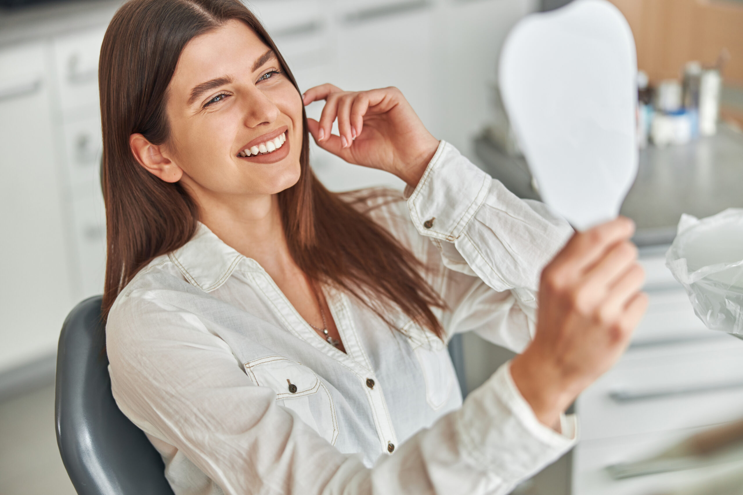 young woman smiling in a mirror sitting in a dental chair, perfect white teeth