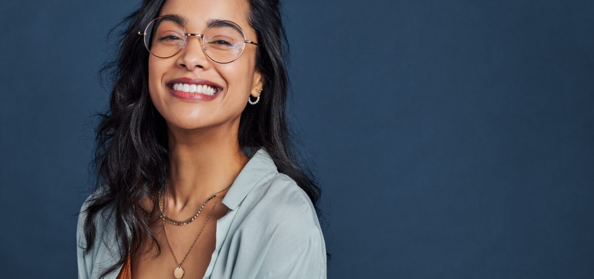 Casual young woman with eyeglasses smiling at camera on blue background, perfect white smile