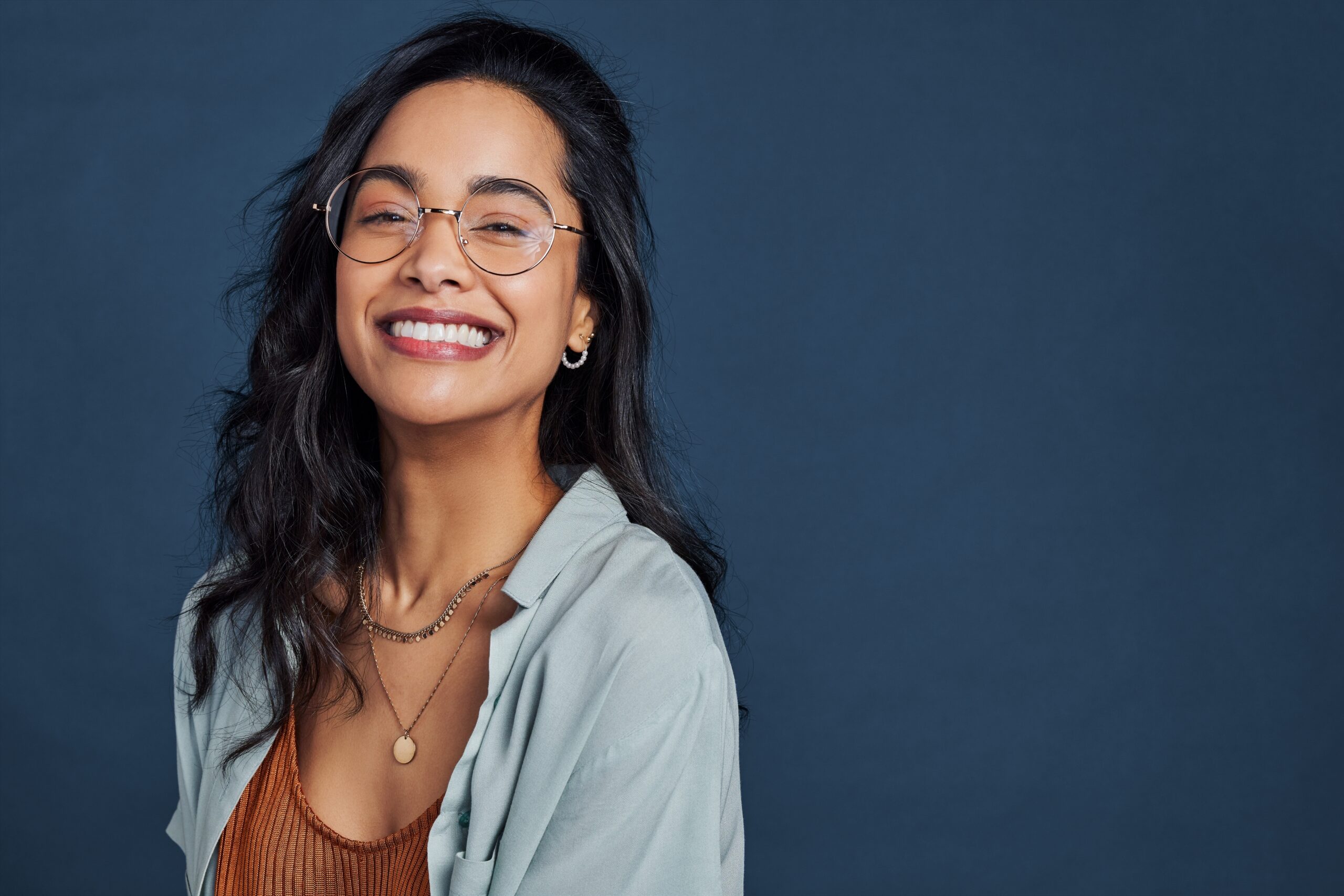 Casual young woman with eyeglasses smiling at camera on blue background, perfect white smile