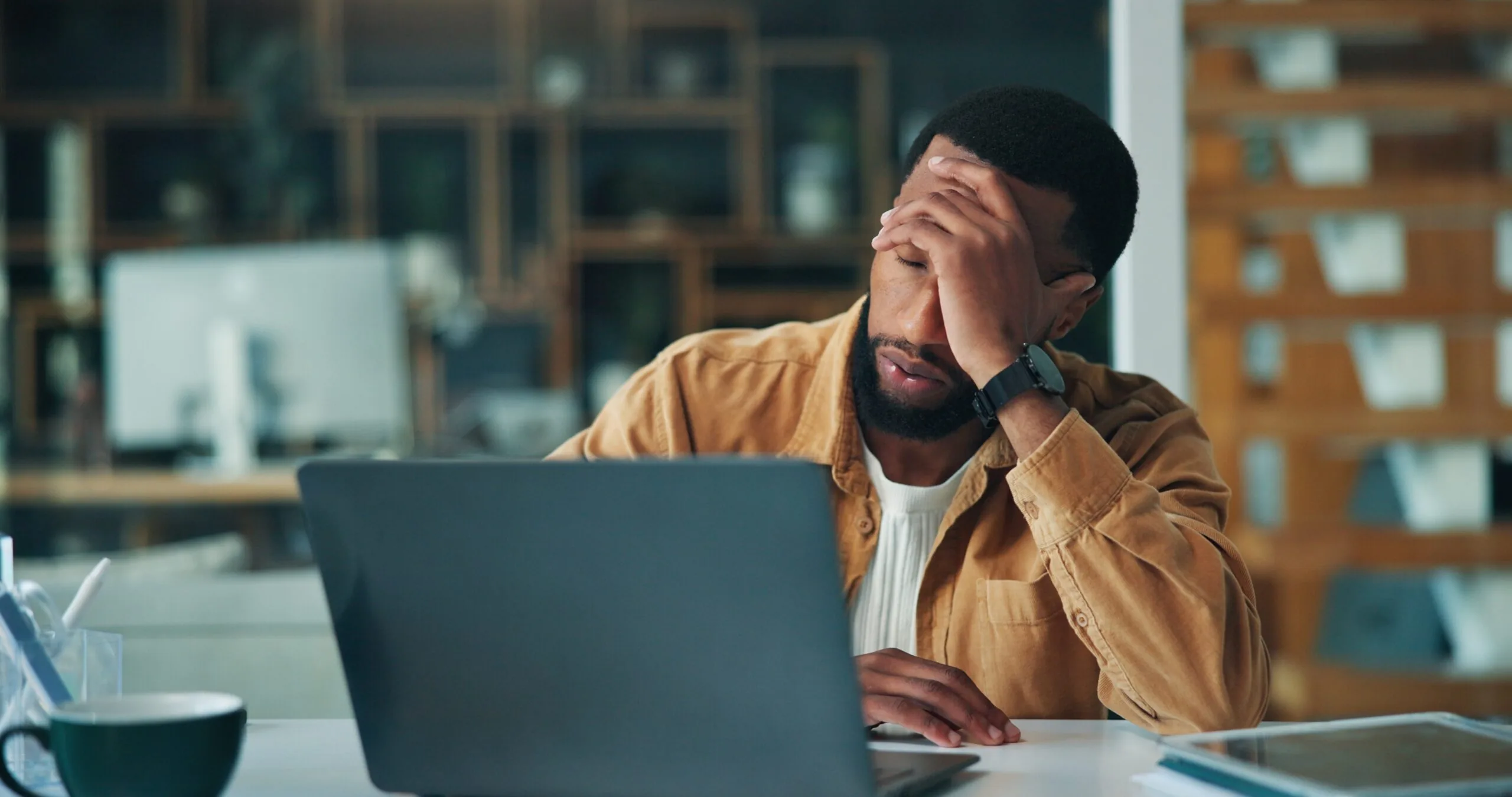fatigued man sitting at his computer, hand over face
