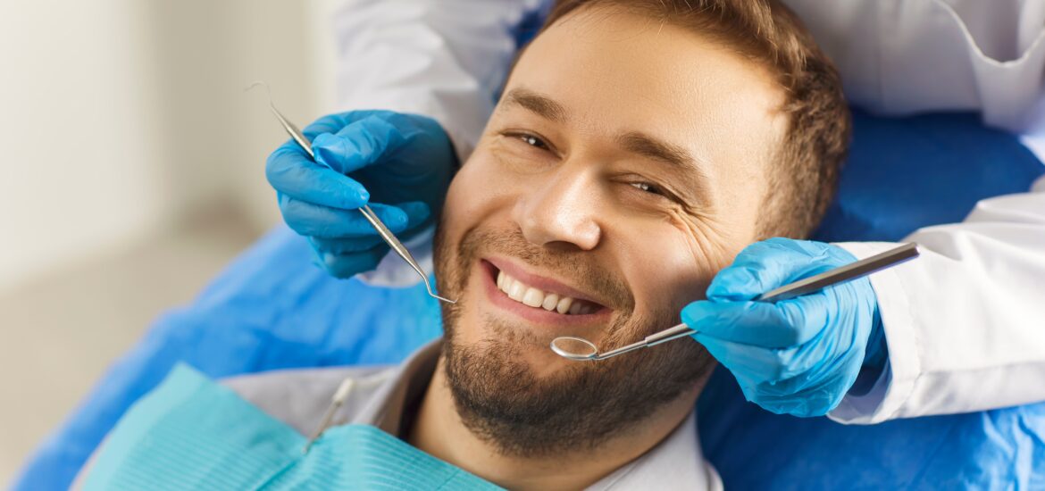 man sits comfortably in the dentist's chair, displaying a white smile that exudes confidence. The dentist has special tools in his hands for the preventive and therapeutic examination of the teeth