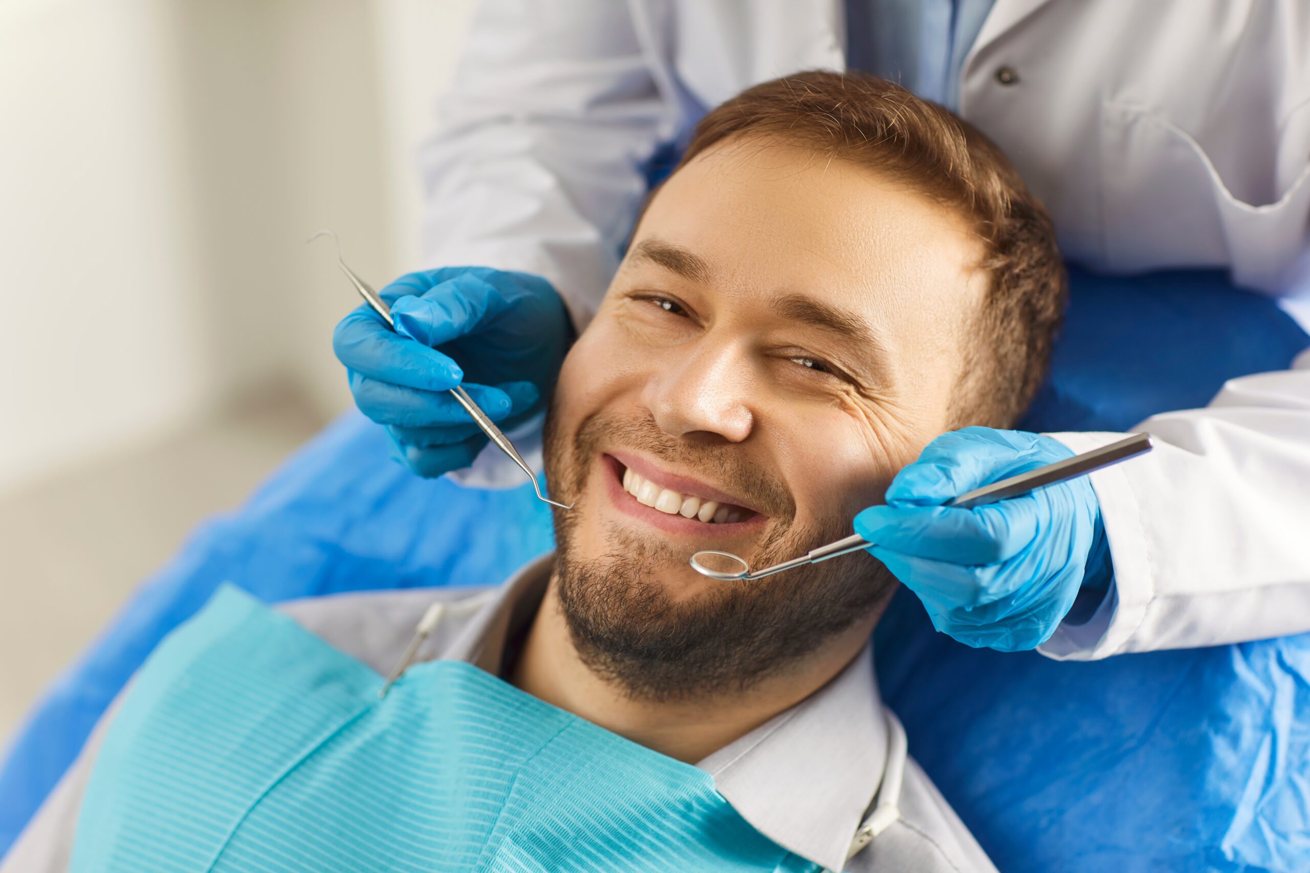 man sits comfortably in the dentist's chair, displaying a white smile that exudes confidence. The dentist has special tools in his hands for the preventive and therapeutic examination of the teeth